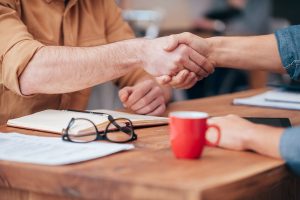 Close-up of two men shaking hands while sitting at the wooden desk